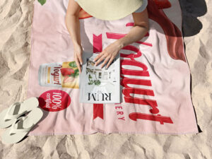 Microfiber Towel with Custom Print. Ideal for events and beach. Pink towel onn the beach where girl has picnic. Buy in amgs group.