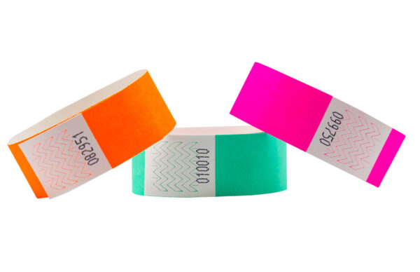 Set of 25mm Tyvek wristbands in orange, green, and pink. Detail view of serial numbering and adhesive zone. Custom Tyvek Wristbands 25 mm. Manufacturer AMGS Group.